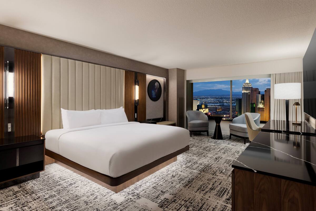 A modern hotel room with a large bed, a desk, and a view of the cityscape.