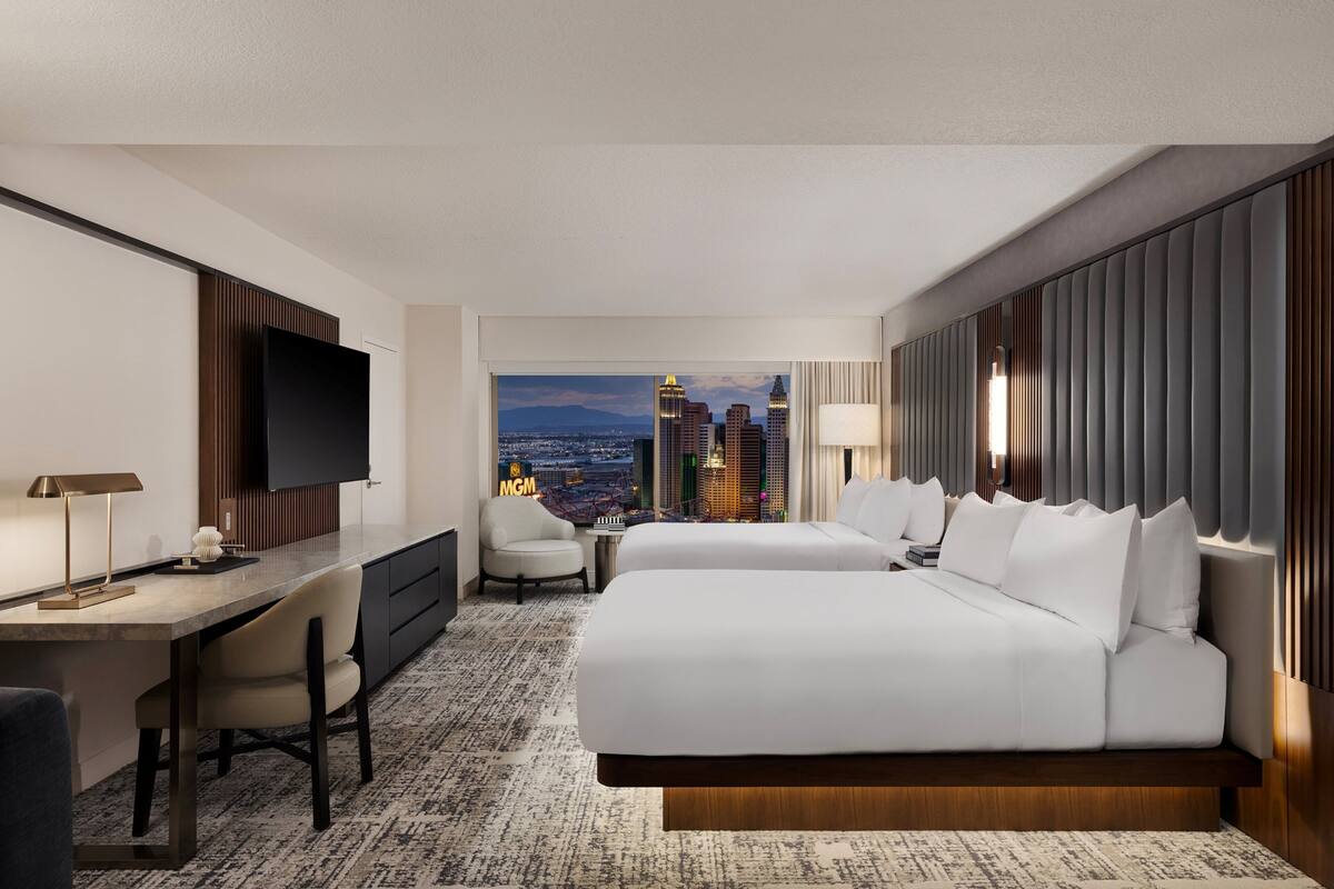 A hotel room with a desk, two beds, a TV, and a city view.