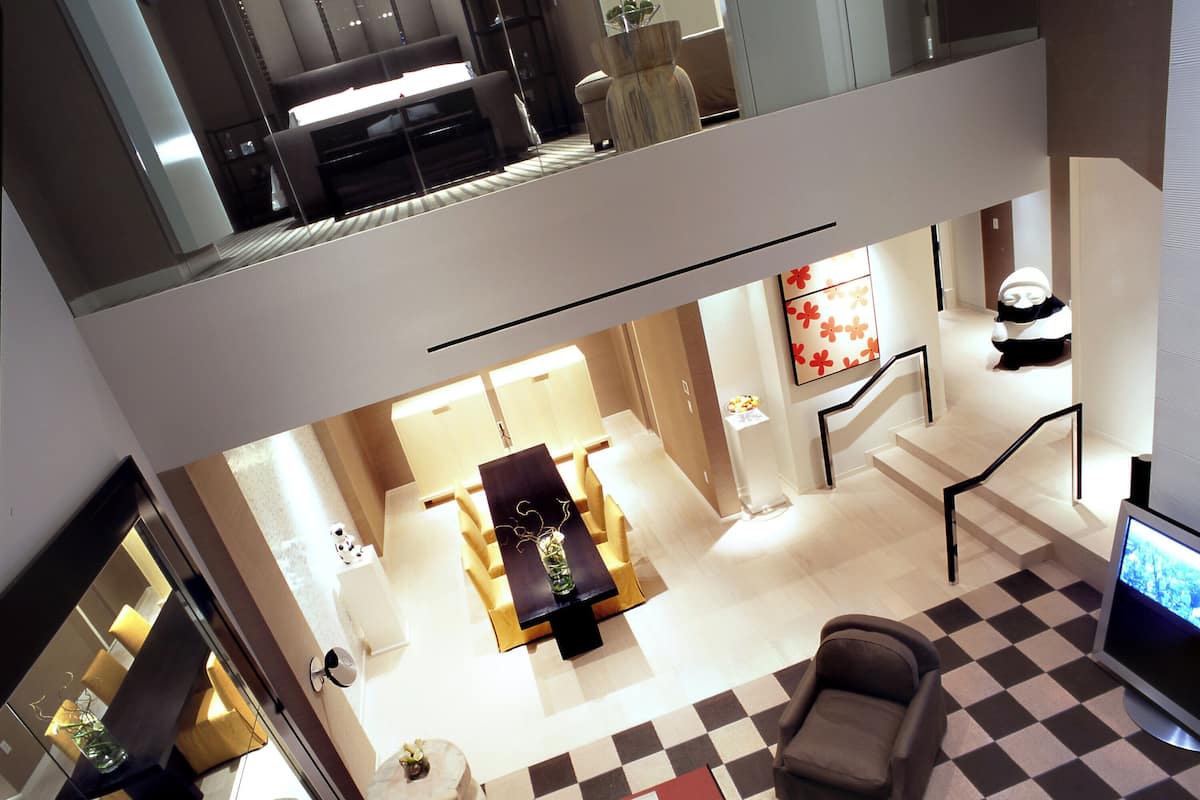 A spacious living area with a high ceiling, a checkered floor, a sofa, a dining table, and a TV.