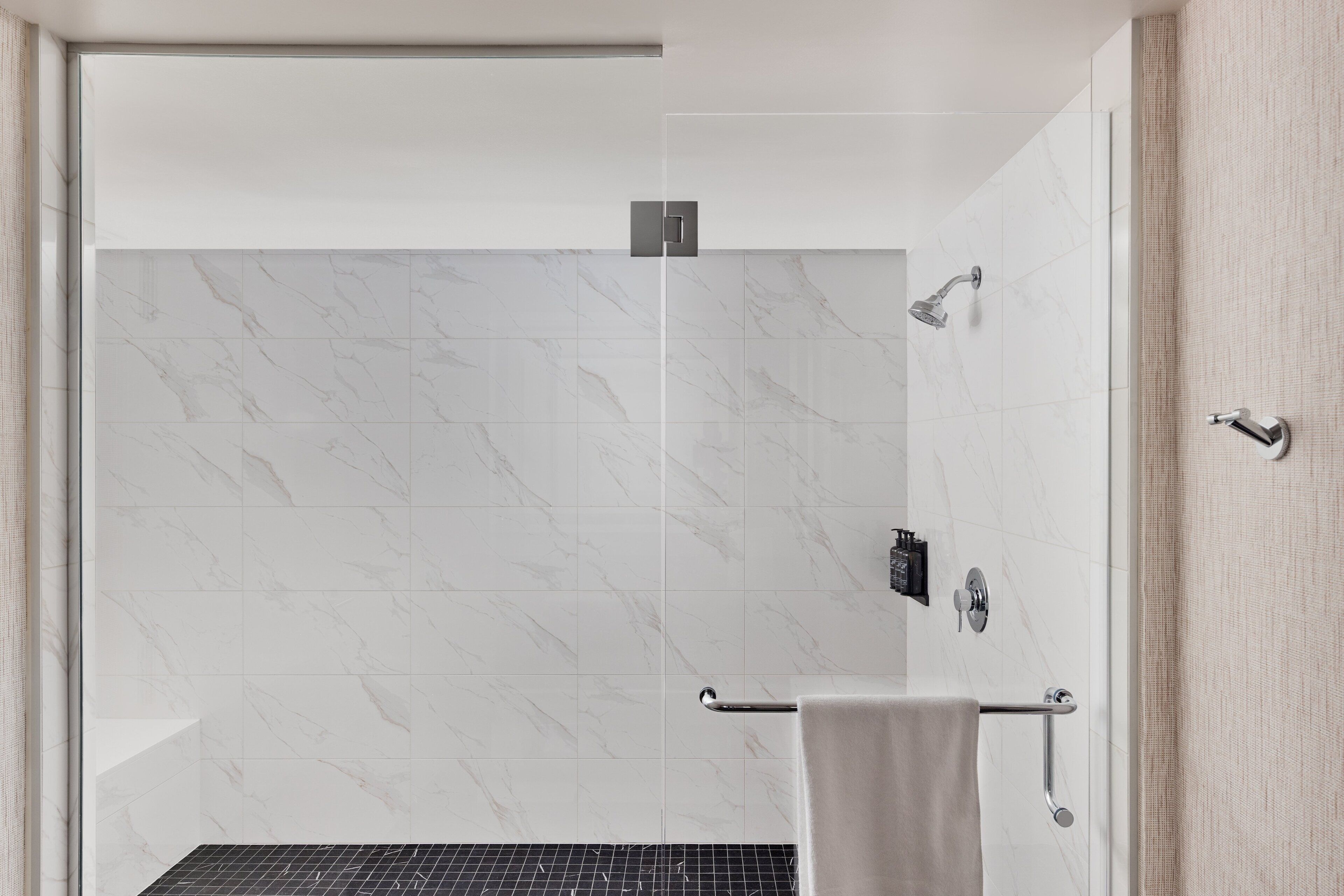 A modern bathroom with a glass shower enclosure, marble tiles, and a towel rack.