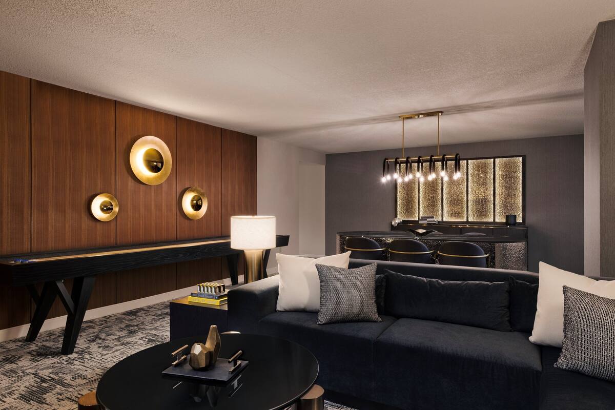 A modern living room with a dark blue sofa, a black coffee table, a wooden piano, and a decorative wall with circular light fixtures.