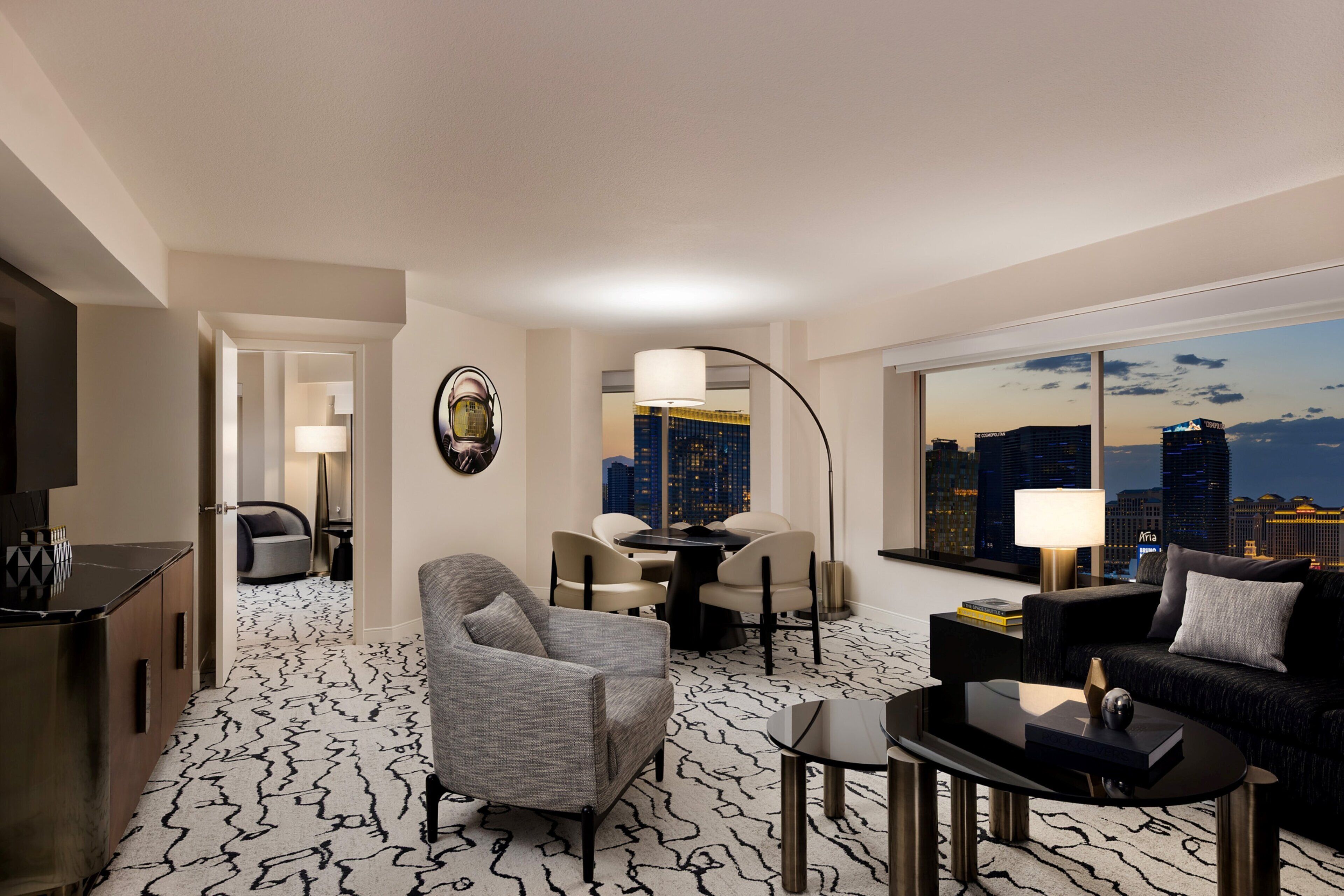 A modern hotel room with a city view, a dining area, and a living space with a sofa and coffee table.