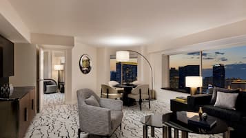 A modern hotel room with a city view, a dining area, and a living space with a sofa and coffee table.