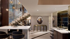 A modern kitchen with a central island, bar stools, a staircase, and a large mirror.