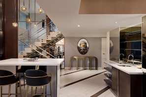 Una cocina moderna con una isla central, taburetes de bar, una escalera y un espejo grande.