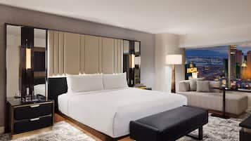 A modern hotel room with a large bed, a bench, a nightstand, a lamp, and a view of the cityscape.