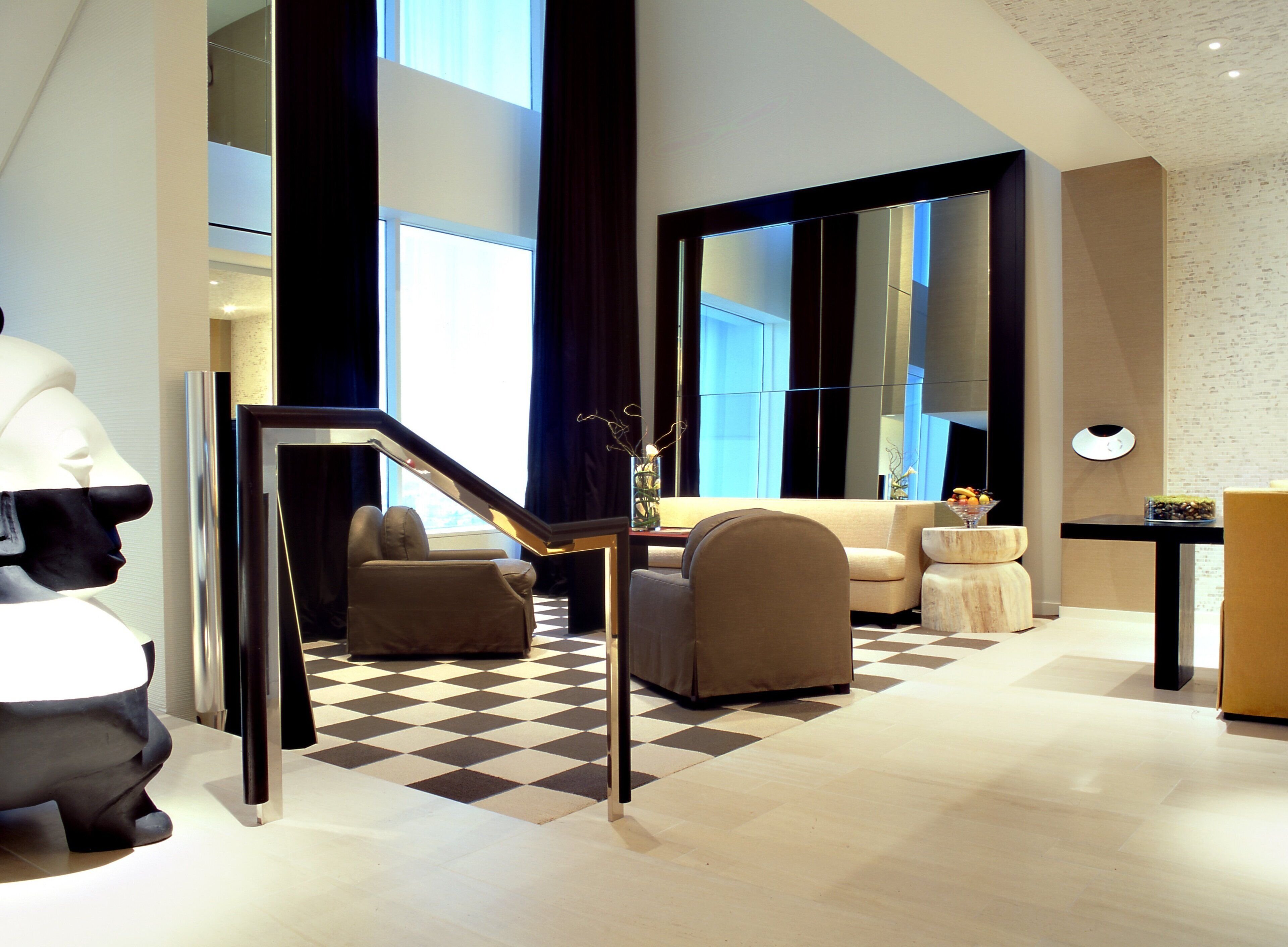 A modern hotel lobby with a checkered floor, a staircase, and a seating area with a sofa and armchairs.