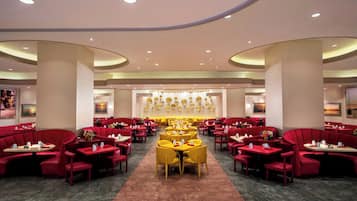 Un vaste espace dédié à la salle à manger, avec des sièges aux couleurs rouge et jaune, de nombreuses tables et un mur décoratif central.