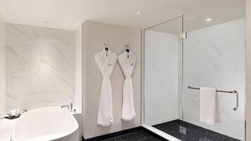 Un baño moderno con una bañera independiente, una ducha con cerramiento de vidrio y dos albornoces blancos colgados en ganchos.