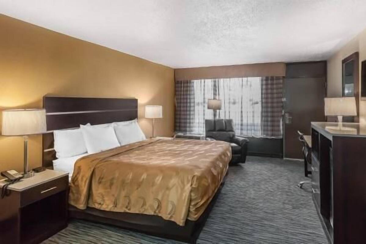A hotel room with a bed, bedside tables, a desk, a chair, and a window with curtains.