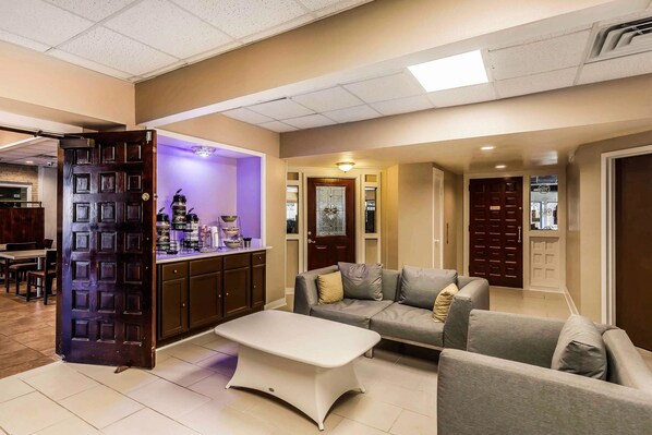 A modern living room with a grey sofa, a white coffee table, and a kitchen area with a purple-lit bar.