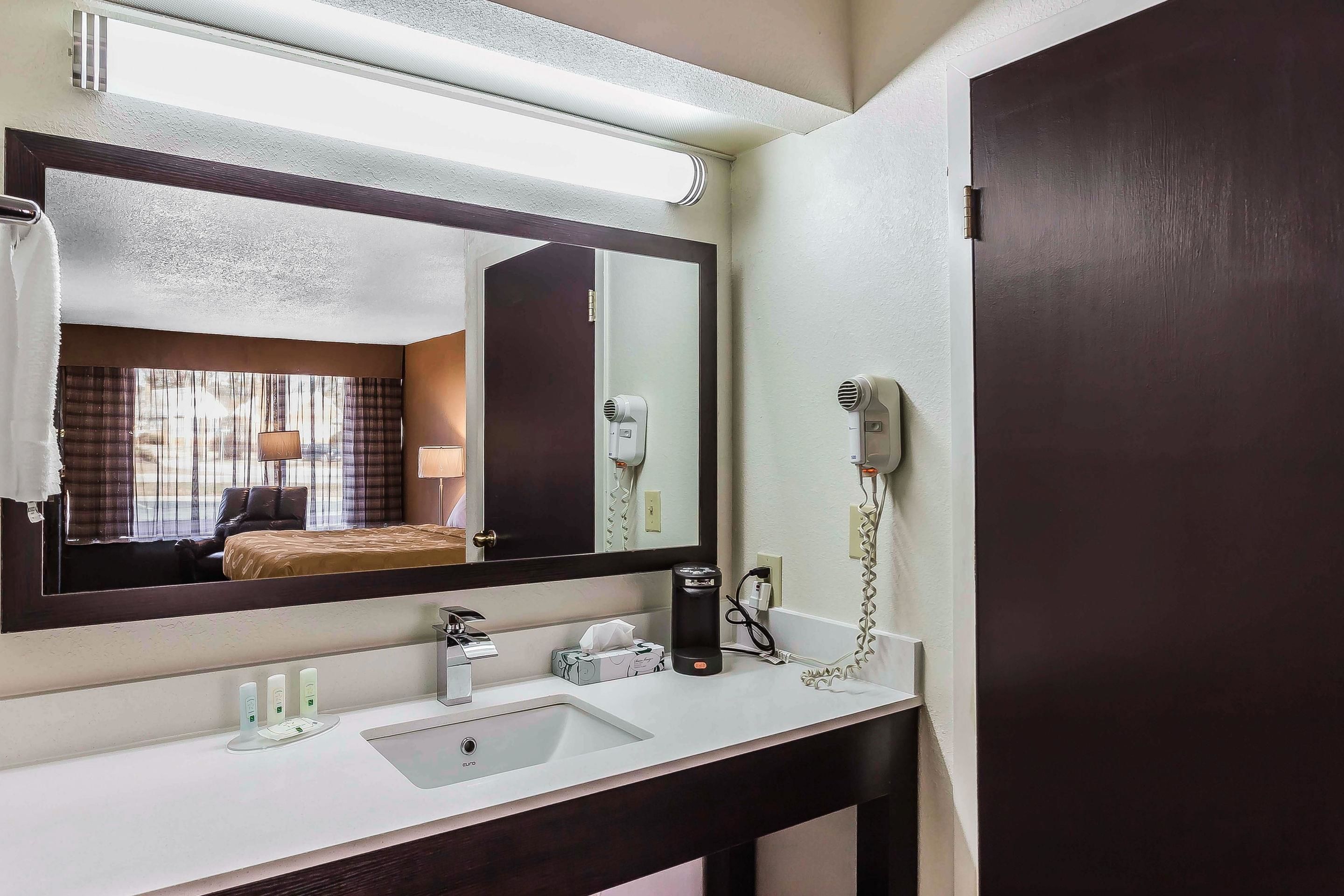 A hotel bathroom with a large mirror, a sink, a hairdryer, and a telephone.