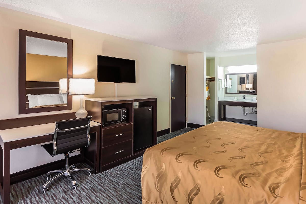 A hotel room with a bed, desk, chair, television, and a small refrigerator.