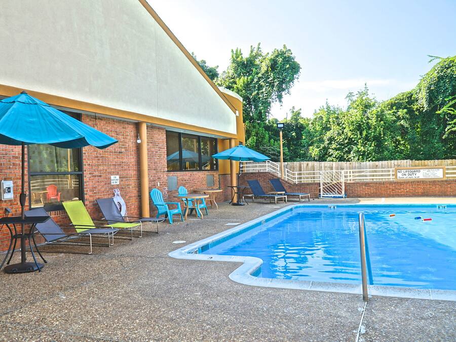 A pool area with lounge chairs and umbrellas, a brick building, and a wooden fence.
