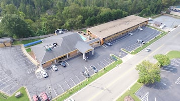 En vy från ovan av en stor byggnad med en parkeringsplats, omgiven av grönska.