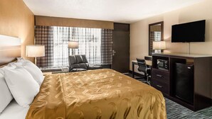 Een hotelkamer met een groot bed, een bureau, een televisie en een raam met gordijnen.