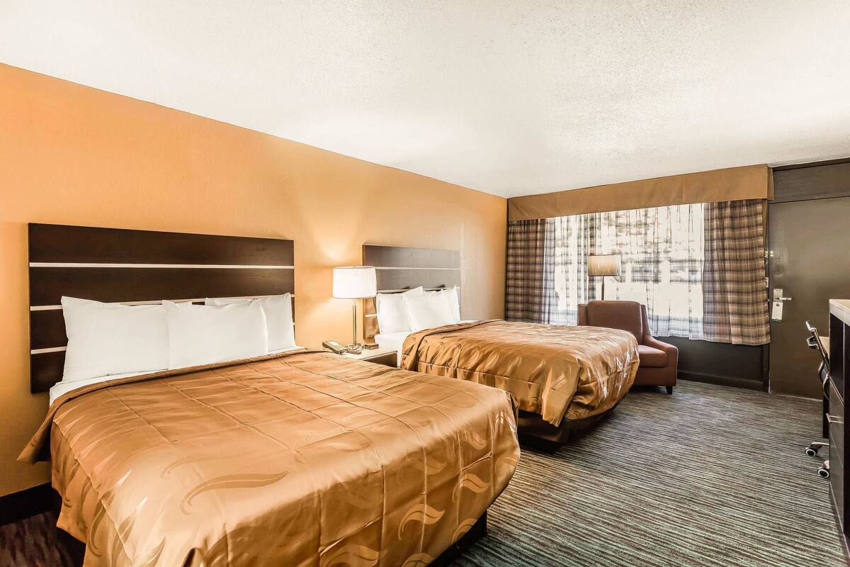 A hotel room with two beds, a desk, a chair, and a window with curtains.