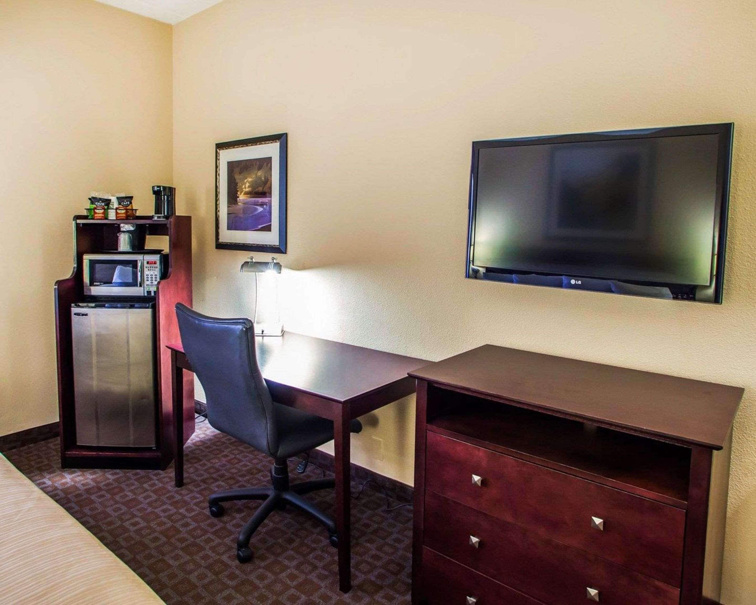A hotel room with a desk, chair, TV, microwave, refrigerator, and a small shelf with snacks.