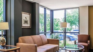 Ein modernes Hotelzimmer mit Ledersofa, einem kleinen Holztisch, einem Glastisch und einem Sessel. Große Fenster bieten einen Ausblick ins Freie.