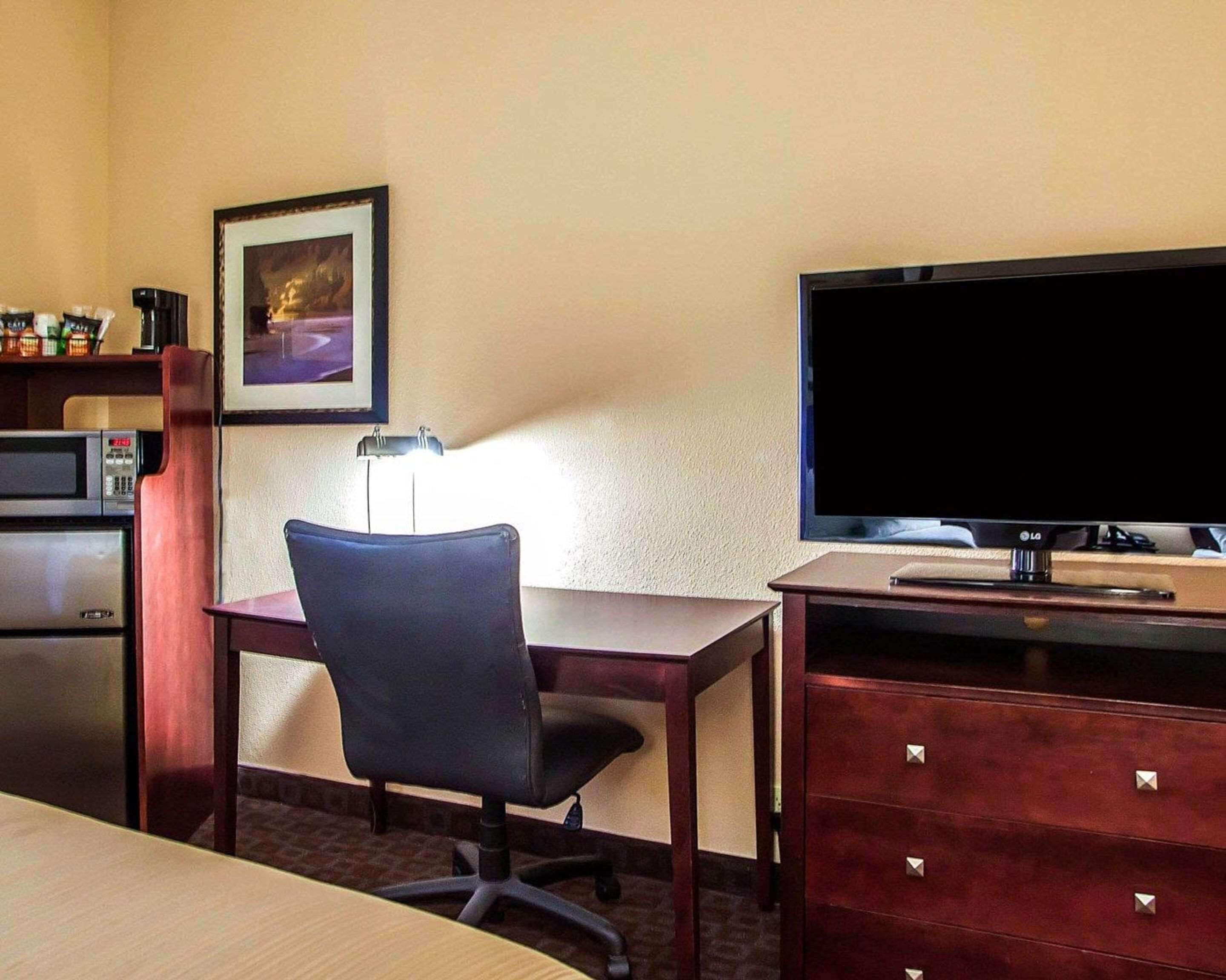 A hotel room with a desk, chair, TV, microwave, and a small cabinet.