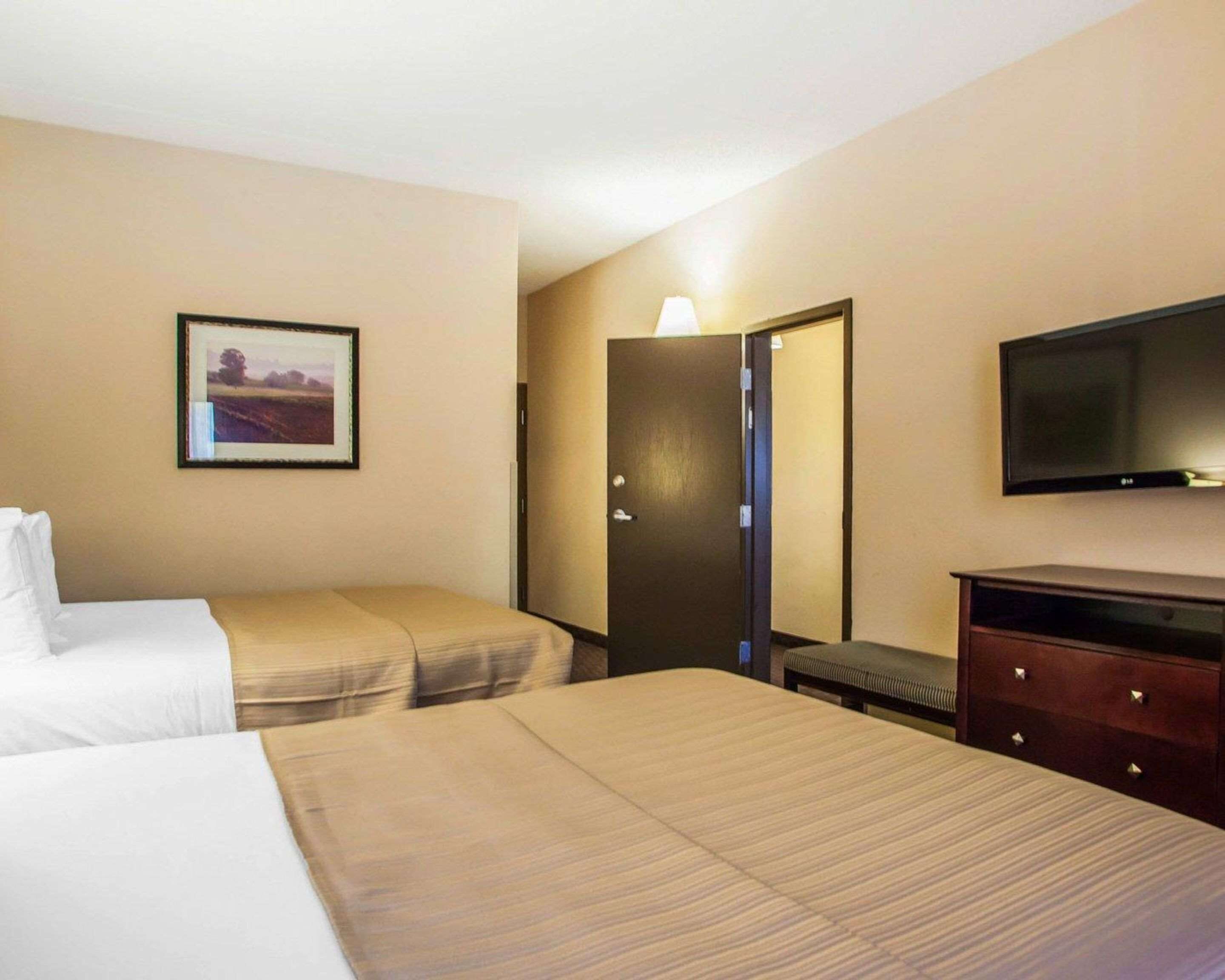 A hotel room with two beds, a television, a dresser, and a door.