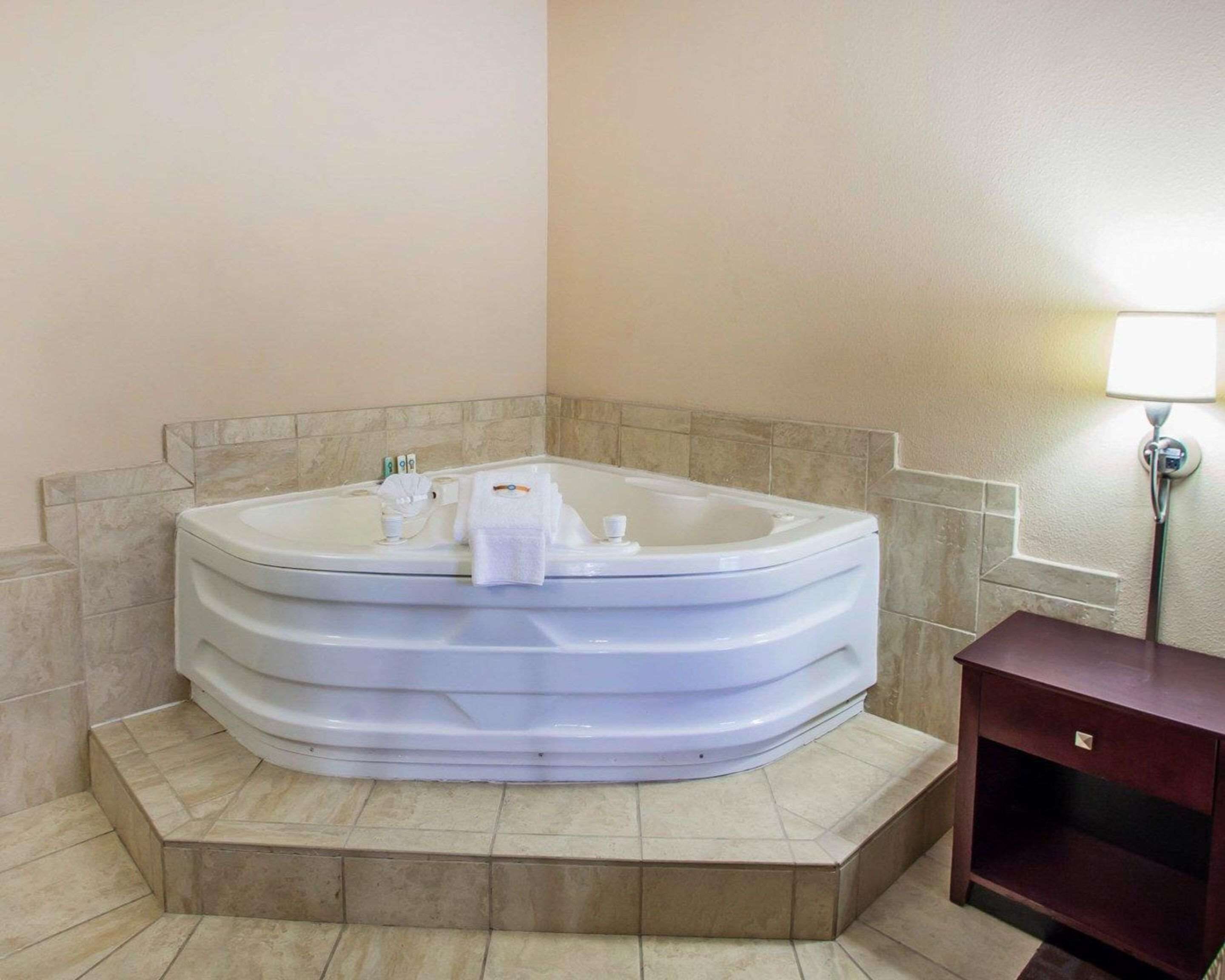 Une petite salle de bain d’angle avec une baignoire sur pieds, un petit meuble en bois et une lampe fixée au mur.