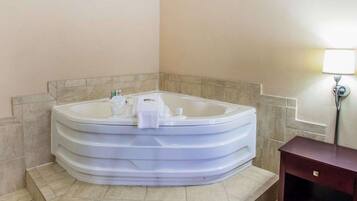 A corner bathroom with a freestanding bathtub, a small wooden cabinet, and a wall-mounted lamp.