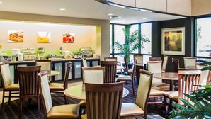 Ein Speisebereich eines Hotels mit runden Tischen und Stühlen, einer Buffettheke und großen Fenstern mit Ausblick.