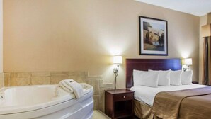 Ein Hotelzimmer mit einer großen Badewanne, einem ordentlich bezogenen Bett und einem gerahmten Bild an der Wand.
