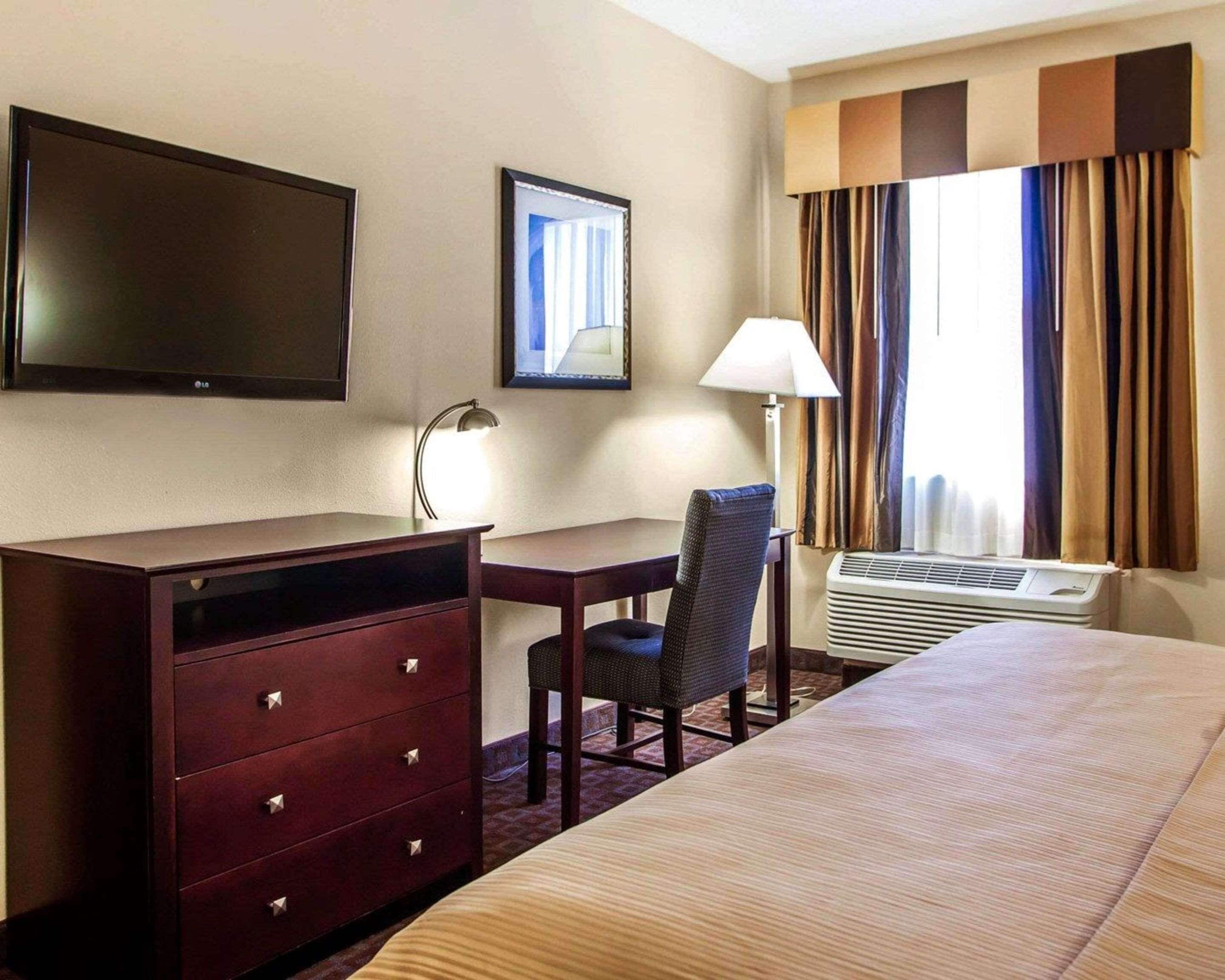Une chambre d’hôtel équipée d’un lit, d’un bureau, d’une chaise, d’une télévision, d’une lampe et d’une fenêtre avec des rideaux.