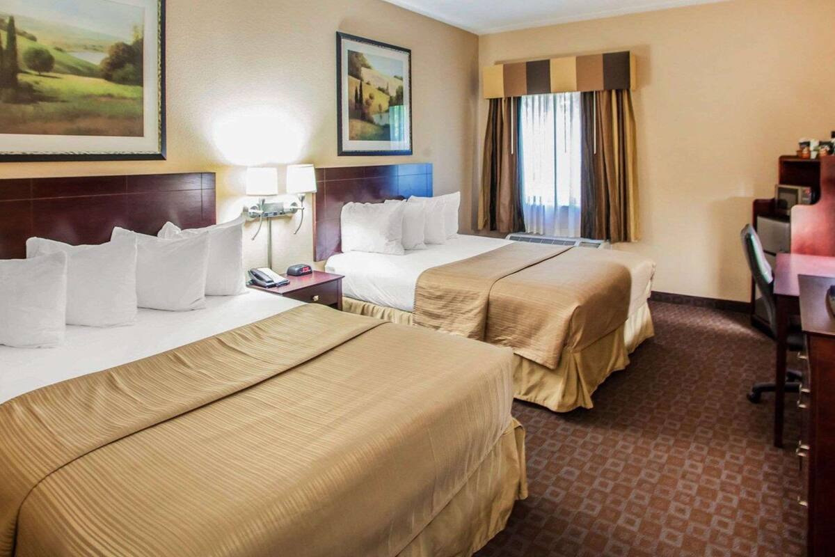 Una habitación de hotel con dos camas, un escritorio, una silla y una ventana con cortinas.