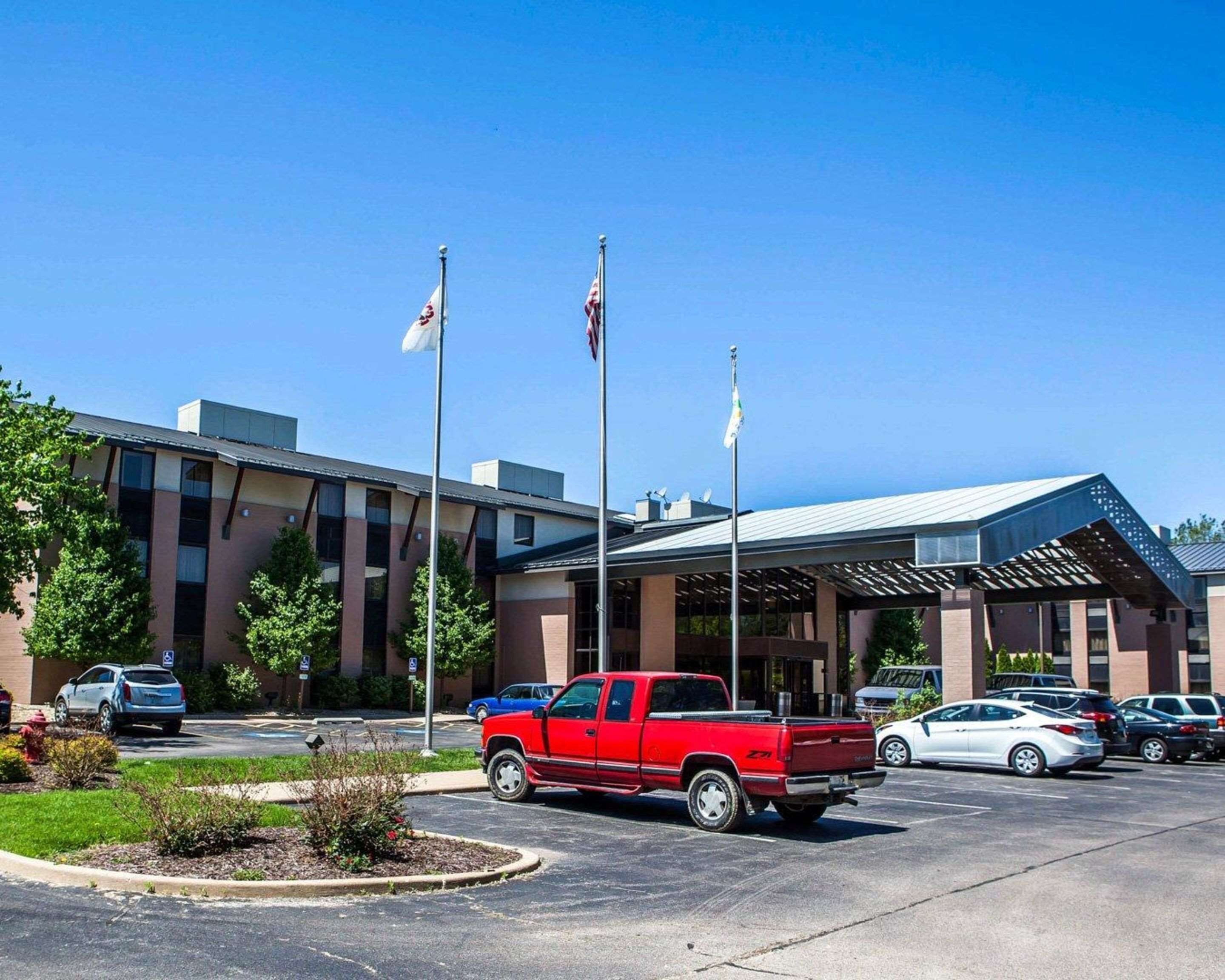 A building with a covered entrance, multiple flags, and a parking lot with various vehicles.