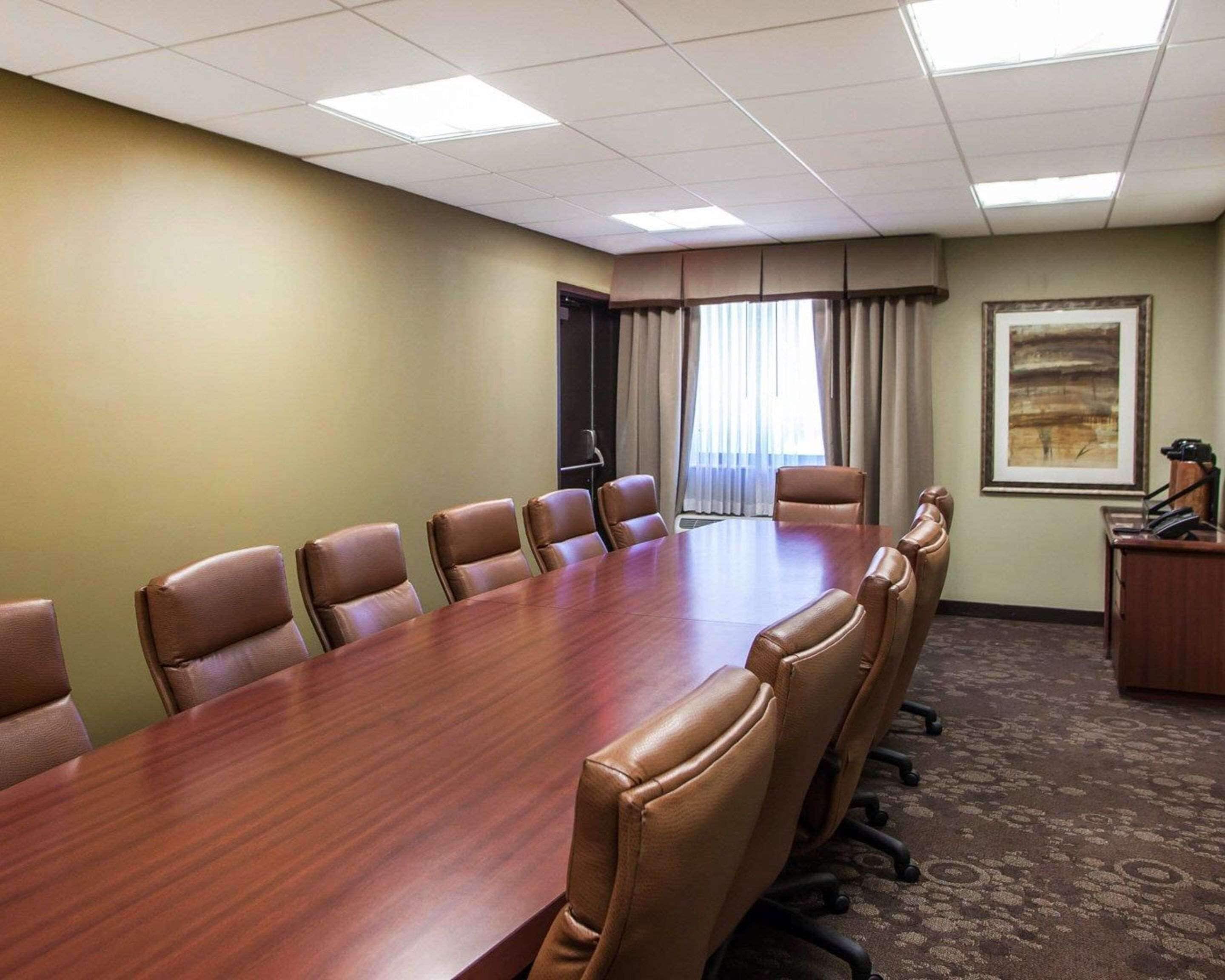 A conference room with a long wooden table surrounded by leather chairs, a carpeted floor, and a painting on the wall.