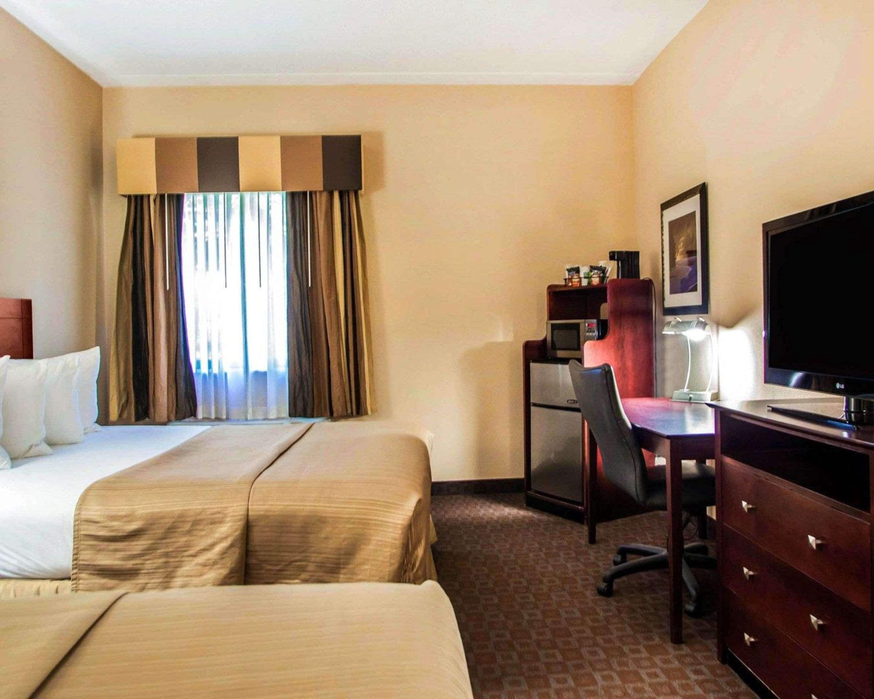 A hotel room with two beds, a desk, a chair, a television, and a minibar.