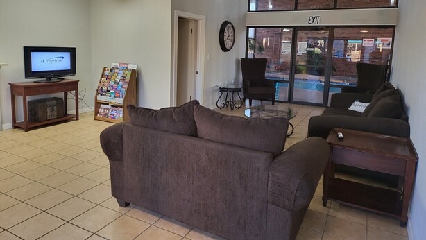 A lobby with a sofa, a TV, a magazine rack, and an exit sign. - Blue Ribbon Inn and Suites (Sallisaw)