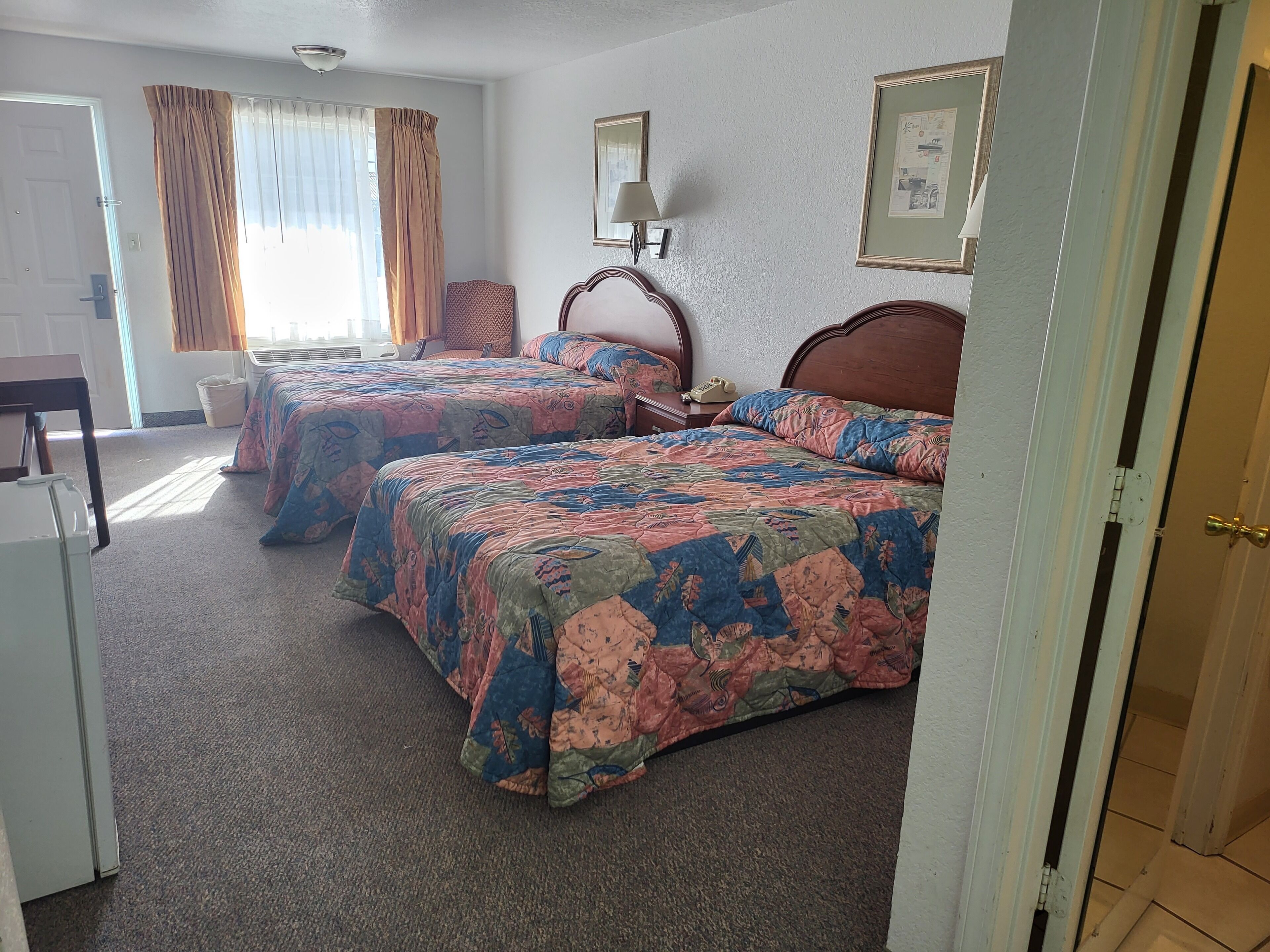 A hotel room with two beds, a desk, and a chair.
