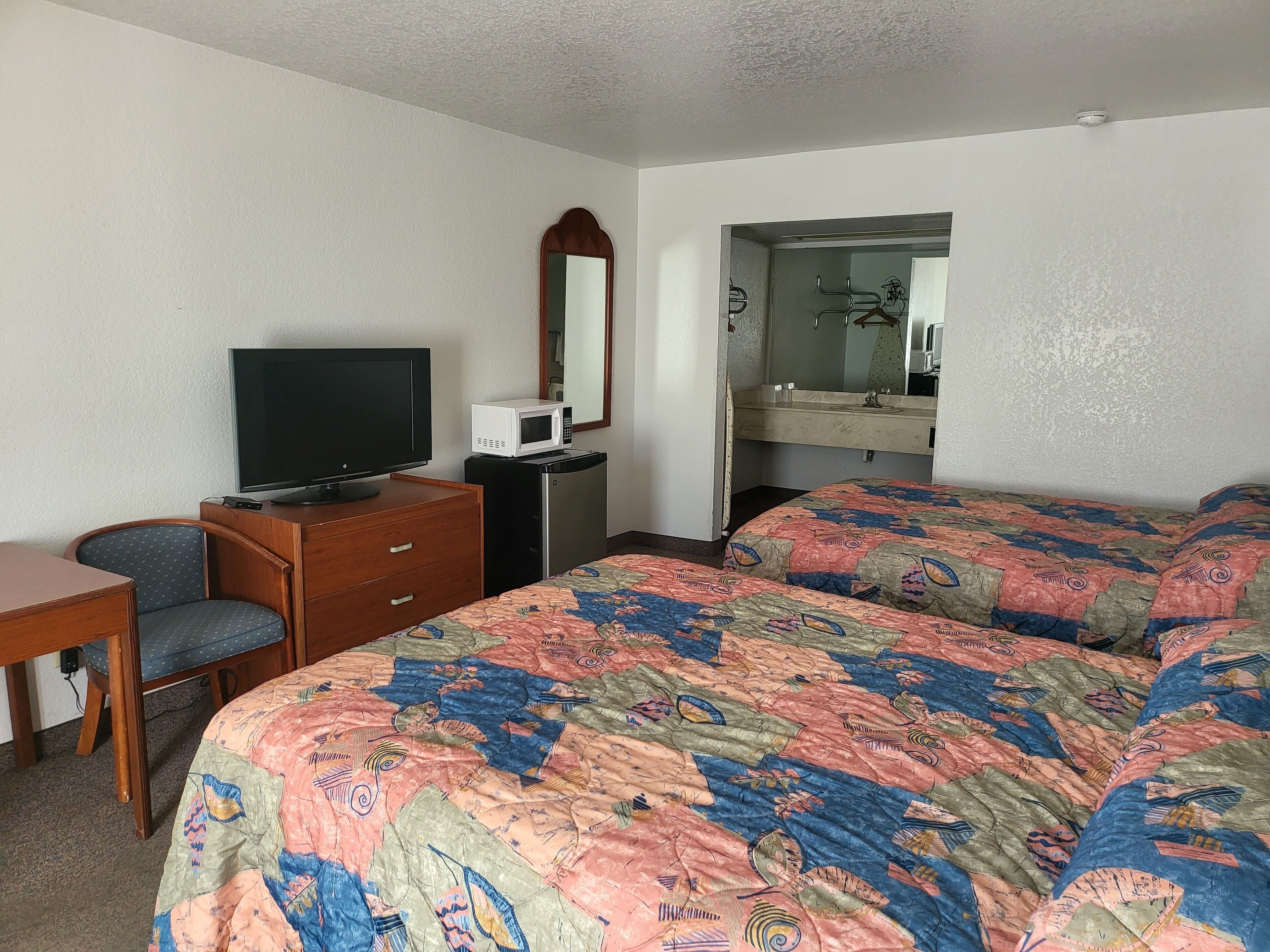 Una habitación de hotel con cama, escritorio, televisión, microondas y espejo.