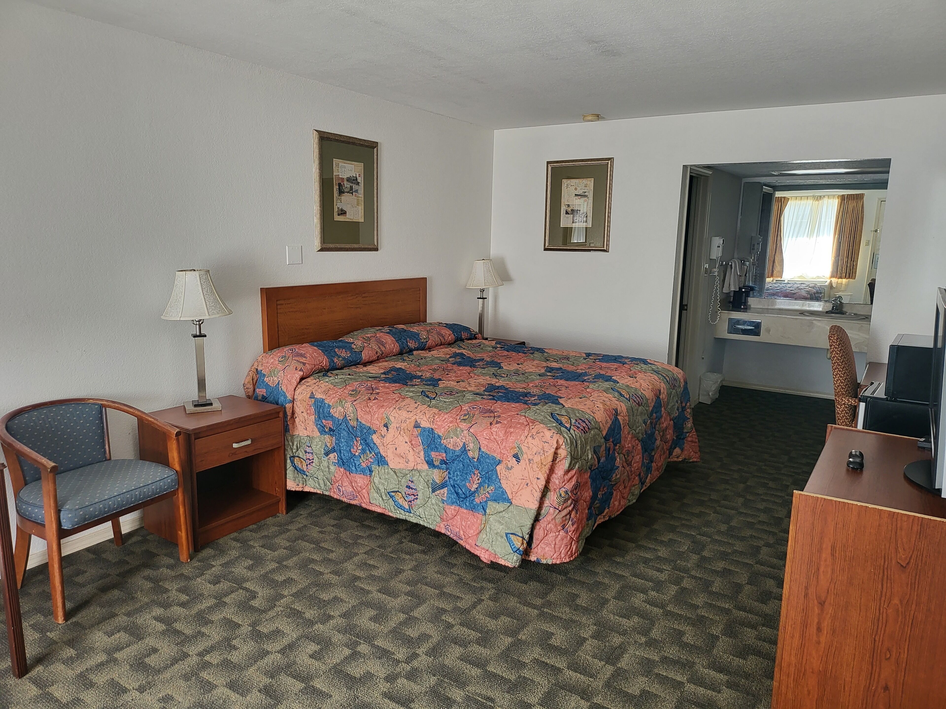 Habitación de hotel con cama, escritorio, silla, lámpara de escritorio, mesita de noche y espejo.