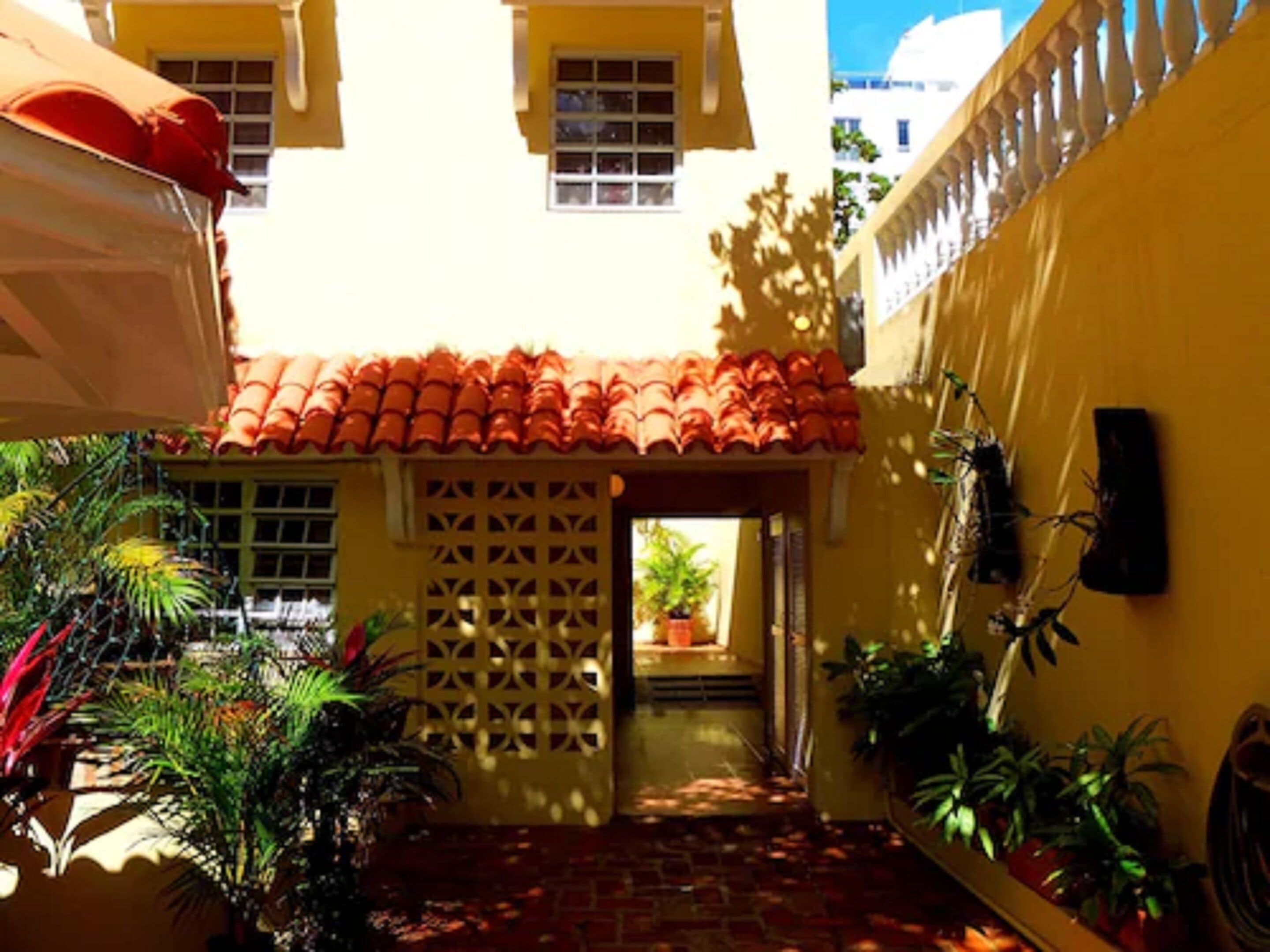 A narrow courtyard with a tiled roof, potted plants, and a lattice door.