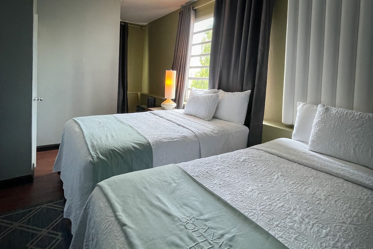 Een hotelkamer met twee bedden, een lamp en een raam met gordijnen.