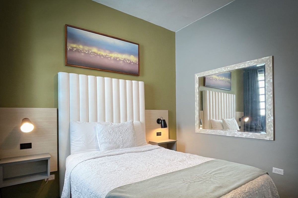 Een keurig opgemaakt hotelkamer met een groot bed, een nachtkastje, een wandspiegel en een schilderij boven het bed.