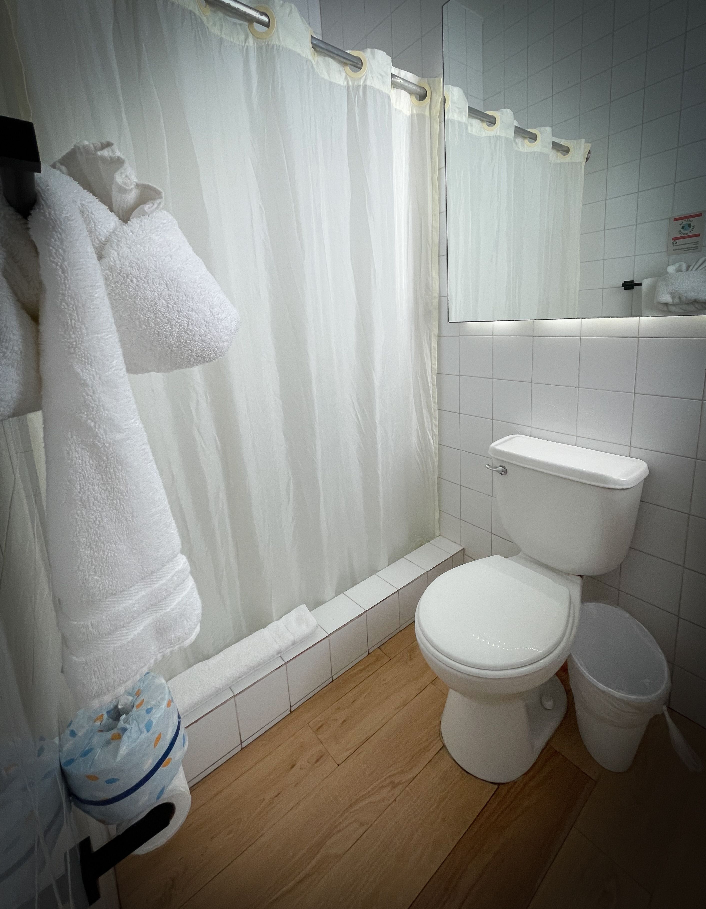 Ein Badezimmer mit Duschvorhang, Toilette, Mülleimer und Handtuchhalter mit Handtüchern.