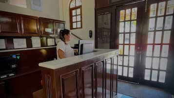Zona de recepción con mostrador de check-in, ventilador de techo y un amplio ventanal con persianas.