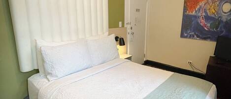 Una cama bien hecha con una colcha blanca y verde clara, un cabecero de madera y un cuadro en la pared.