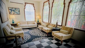 A living room with a checkered floor, a ceiling fan, and a large window with decorative iron bars.
