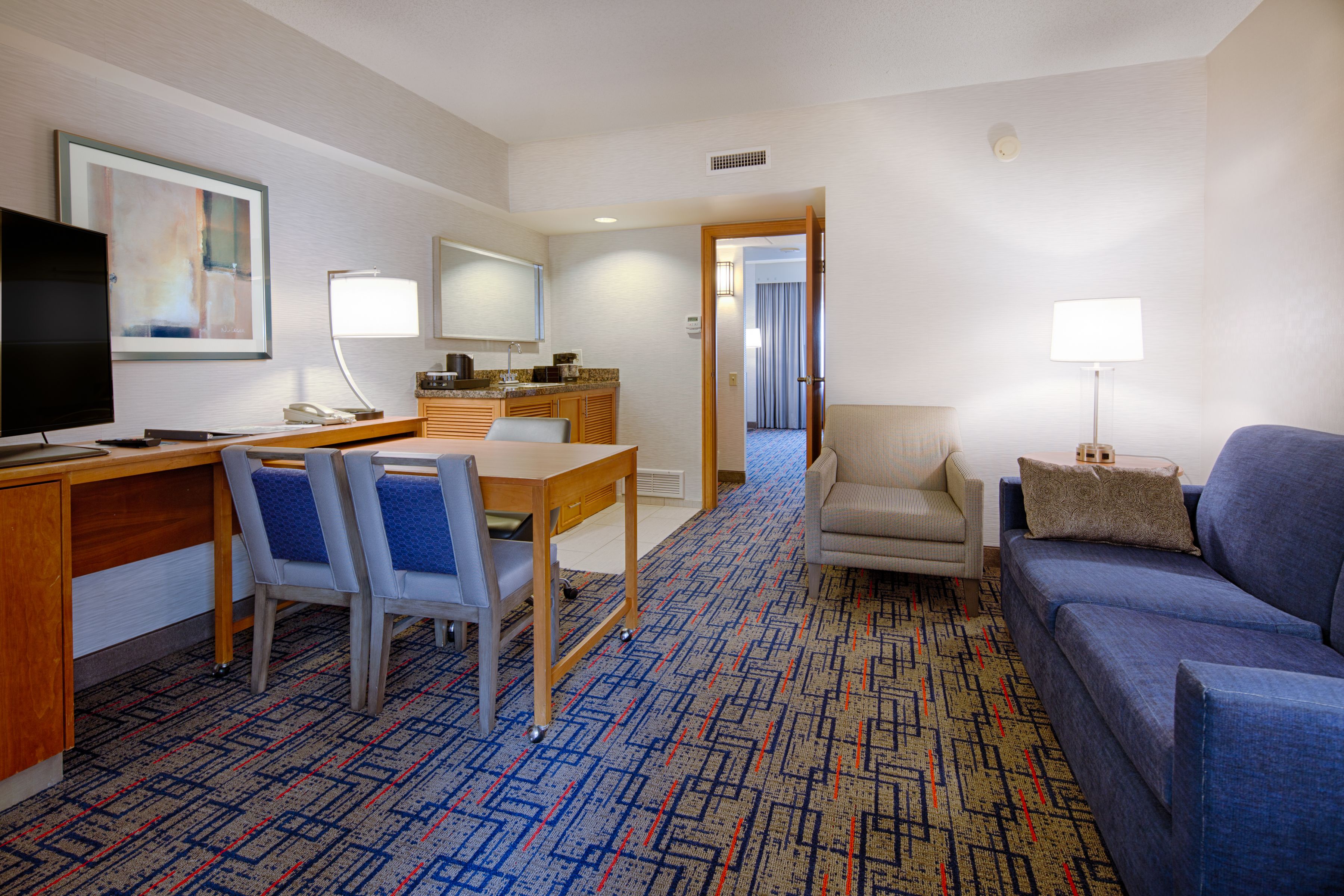Habitación de hotel con comedor, sofá y televisor.