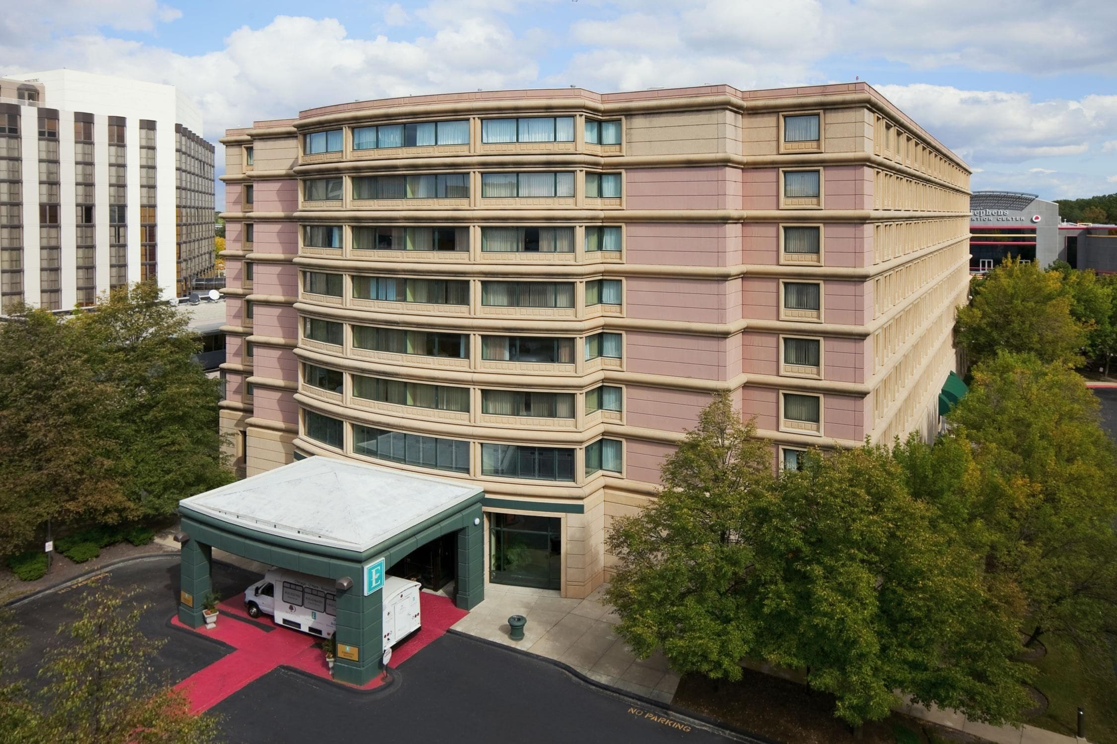 A multi-story hotel with a curved facade, a covered entrance, and a parking area.