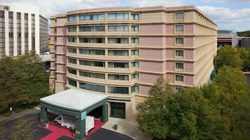 A multi-story hotel with a curved facade, a covered entrance, and a parking area.