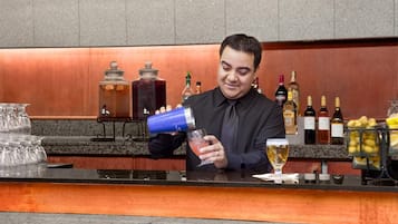 En bartender som gör i ordning en drink bakom bardisken, med olika flaskor och ett fruktfat synligt.
