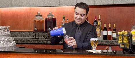 Un cantinero preparando una bebida detrás de la barra, con varias botellas y una presentación de frutas.